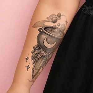 Könnte beinhalten: Schwarz-weiß-Tattoo eines Kessels mit einem Mond, Blasen und Rauch. Der Kessel sitzt auf einer Kristallformation mit zwei Sternen. Das Tattoo befindet sich auf dem Arm einer Person.