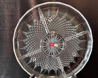 May include: Clear glass serving dish with a starburst design. The dish is divided into five sections and has a textured surface. The center of the dish has a circular design with a red and white label.