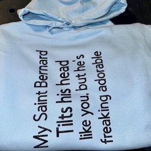 Cute Saint Bernard Hoodie print on both sides. The wording “My Saint Bernard tilts his head like you, but he’s freaking adorable “ front