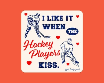 Könnte beinhalten: Quadratischer Aufkleber mit orangefarbenem Hintergrund. Der Aufkleber hat ein cremefarbenes Quadrat mit zwei Eishockeyspielern in Blau und Weiß. Der Text lautet „I LIKE IT WHEN THE Hockey Players KISS“. Rote Herzen sind um den Text verstreut.