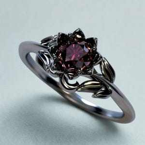 以下が含まれることがあります： 深い赤色の宝石を中央に配した、花型のセッティングが特徴のシルバーリング。 リングのバンドと花の装飾は、自然にインスパイアされたデザインです。 リングには葉のような装飾が施されています。