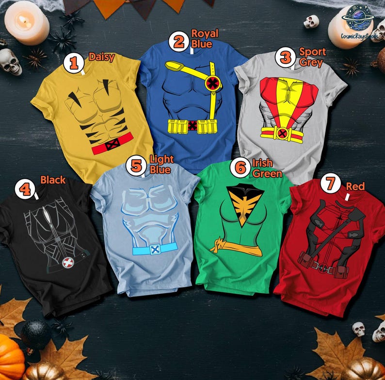 Puede incluir: Siete camisetas de manga corta en varios colores, cada una con un dise&ntilde;o de disfraz de superh&eacute;roe. Los colores incluyen amarillo, azul, gris, negro, azul claro, verde y rojo. Las camisetas est&aacute;n dispuestas sobre una superficie oscura con decoraciones de Halloween.