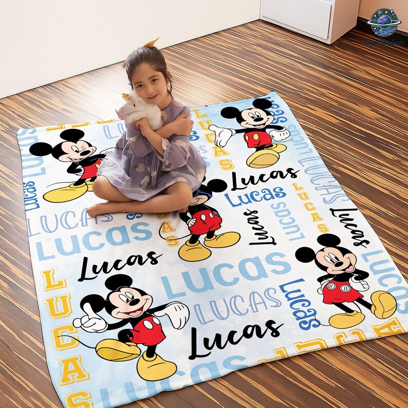 A young girl sitting on a Mickey Mouse-themed blanket with the name "Lucas" written on it.