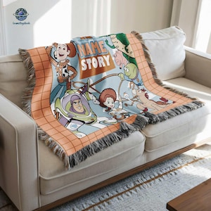 A colorful, cartoon-style blanket with characters from the Toy Story movie, including Woody, Buzz Lightyear, and other beloved characters, is draped over a white couch.