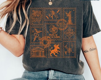 Puede incluir: Una camiseta gris oscuro con un estampado naranja de sellos con varios símbolos y el texto "Percy Jackson".