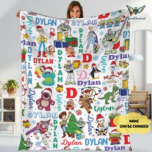 May include: A white fleece blanket featuring various Toy Story characters in festive holiday attire. The blanket is decorated with the name "Dylan" and Christmas-themed elements like snowflakes and presents. The name can be changed.