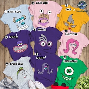 May include: A collection of nine short-sleeve t-shirts in various colors, each featuring a unique cartoon monster face graphic. The shirts are light blue, light pink, gold, purple, sport grey, and irish green, displaying diverse creature designs.