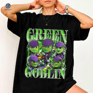 A person wearing a black t-shirt with a graphic design featuring a group of green-skinned, purple-haired characters with the text "GREEN GOBLIN" prominently displayed.