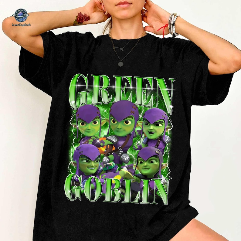 A person wearing a black t-shirt with a graphic design featuring a group of green-skinned, purple-haired characters with the text "GREEN GOBLIN" prominently displayed.
