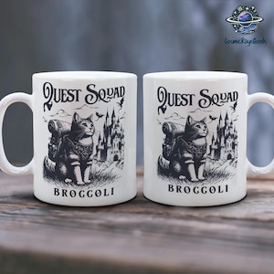 May include: Two white ceramic mugs with black illustrations of a cat wearing a backpack and carrying a sword. The mugs have the text "Quest Squad Broccoli" on the front.