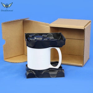 May include: A white ceramic mug with a black protective insert inside a brown cardboard box. The mug is sitting on a black foam insert.