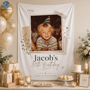 May include: A white fabric birthday banner featuring a central photograph of a child wearing a party hat, the text 1996, Jacob's 30th Birthday, and Aged to Perfection, decorated with botanical illustrations and tape accents on a white background.