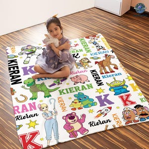 A young girl is sitting on a colorful blanket with various cartoon characters and characters from the Toy Story movie.