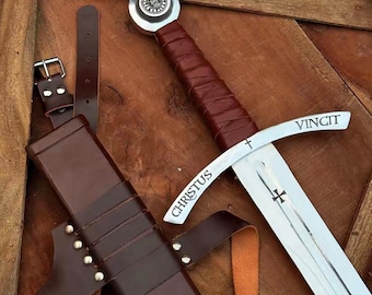 May include: A medieval sword with a silver blade and a brown leather-wrapped handle. The sword has the word "CHRISTUS" and "VINCIT" etched on the blade. A brown leather sheath and belt are also present.