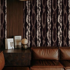May include: A room interior featuring a brown leather sofa, a dark wooden side table with books and a decorative lamp, and a wall with a dark brown and beige patterned wallpaper. The overall aesthetic is modern and sophisticated.