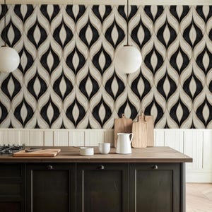 May include: A kitchen with a black and wood-toned island, featuring a stove, cutting boards, and white ceramic items. The backdrop is a wallpaper with a black, beige, and white teardrop pattern. Two white globe pendant lights hang above the island.