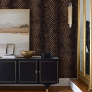 May include: A room interior featuring a black cabinet with gold trim, a gold decorative bowl, and a framed painting. The wall is covered in a textured, brown snakeskin pattern. A gold-framed mirror and a wall sconce with hanging crystals are also visible.