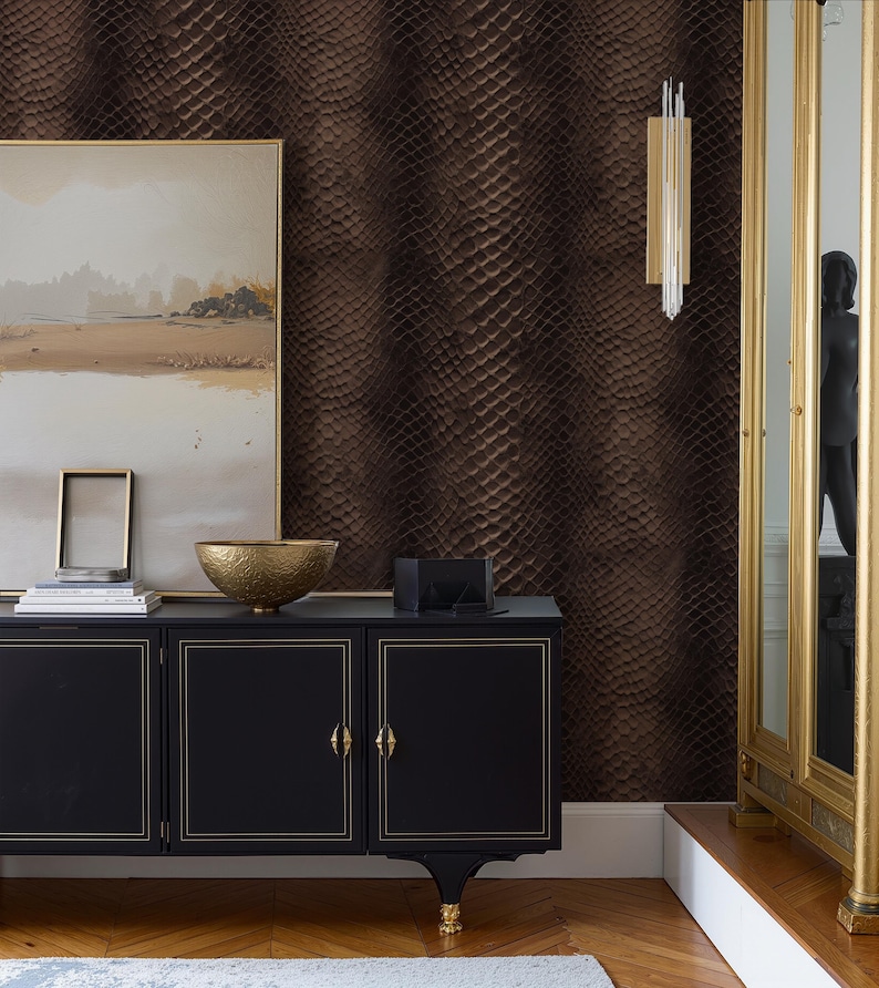 May include: A room interior featuring a black cabinet with gold trim, a gold decorative bowl, and a framed painting. The wall is covered in a textured, brown snakeskin pattern. A gold-framed mirror and a wall sconce with hanging crystals are also visible.