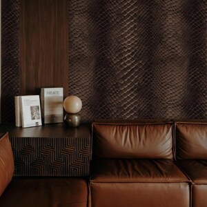 May include: A living room scene featuring a brown leather sofa, a dark wood side table with books and a decorative sphere, and a wall with a snakeskin pattern. The color palette is dominated by shades of brown and dark wood.