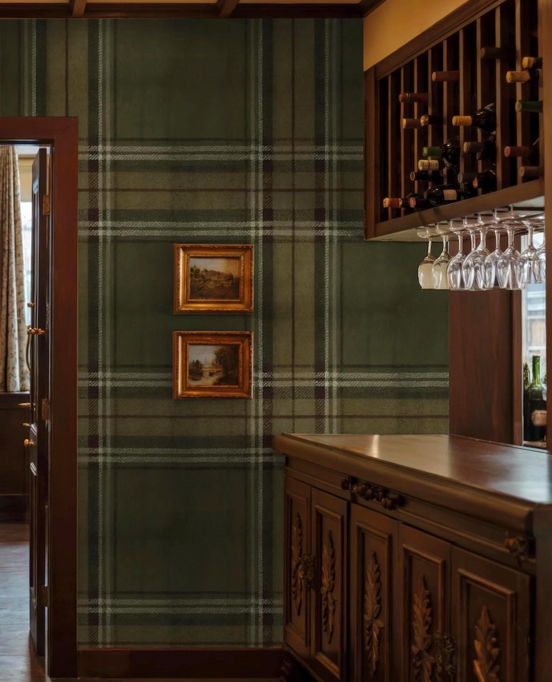 May include: Interior view of a room with green plaid wallpaper and two framed landscape paintings. A wooden bar area includes a wine rack, hanging glasses, and a cabinet with carvings. The door frame is dark wood.
