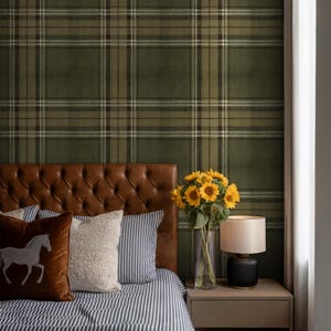 May include: A bedroom interior with a brown leather headboard, striped bedding, and decorative pillows. A vase of sunflowers and a lamp are on a bedside table. The wall is covered in green plaid wallpaper.