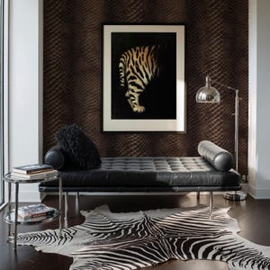May include: A modern living room featuring a black leather chaise lounge, a zebra-print rug, and a framed artwork of a tiger. A chrome side table holds books, and a silver floor lamp provides light. The wall has a textured, dark brown pattern.