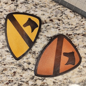 May include: Two leather patches with a horse head design and a black stripe. The patches are yellow and brown.