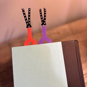 Peut inclure: Deux marque-pages color&eacute;s avec un ruban &agrave; pois noirs et blancs. Les marque-pages sont attach&eacute;s &agrave; un livre avec une page bleu clair et une couverture marron fonc&eacute;.