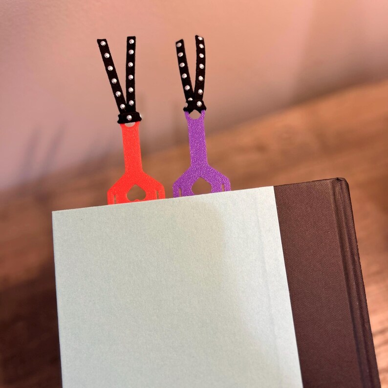 Peut inclure: Deux marque-pages color&eacute;s avec un ruban &agrave; pois noirs et blancs. Les marque-pages sont attach&eacute;s &agrave; un livre avec une page bleu clair et une couverture marron fonc&eacute;.