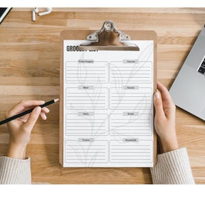 Op de afbeelding: Een wit clipboard met een zwarte clip en de tekst "Grocery List" bovenaan. Het clipboard is verdeeld in secties voor "Produce/Veggies", "Meat", "Dairy", "Frozen", "Drinks", "Baked" en "Household".