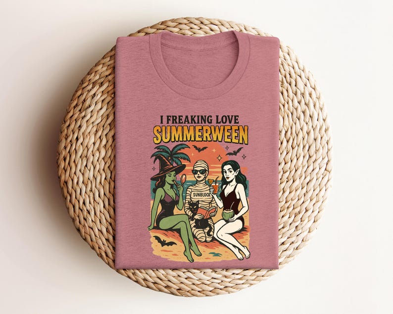 May include: A dusty rose t-shirt with the words "I Freaking Love Summerween" above a graphic of three figures on a beach. The figures include a witch, a mummy, and a woman in a swimsuit, with bats and palm trees.