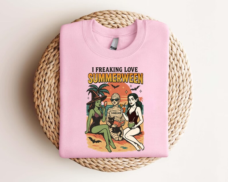 May include: Pink sweatshirt with the text "I Freaking Love Summerween" and a graphic of three women dressed as a witch, mummy, and vampire on a beach. The graphic includes palm trees, bats, and a black cat.