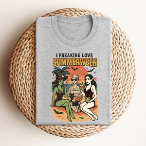 May include: A heather gray t-shirt with the words "I Freaking Love Summerween" above a colorful graphic. The graphic depicts three figures in swimwear, a black cat, palm trees, bats, and the word "Sunblock".