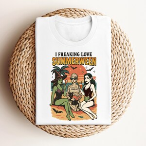 May include: White t-shirt with a graphic featuring three cartoon figures in swimwear on a beach, with the text "I Freaking Love Summerween." The design includes bats, palm trees, and a sunset.