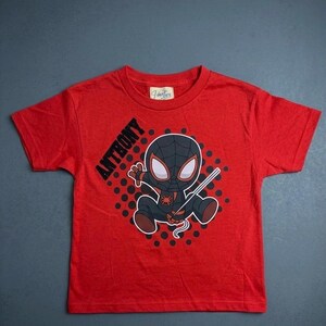 May include: Red t-shirt featuring a cartoon Spider-Man character with the name "ANTHONY" printed on the left side. The graphic includes a black and gray Spider-Man design with a web. The shirt is made of a soft material.