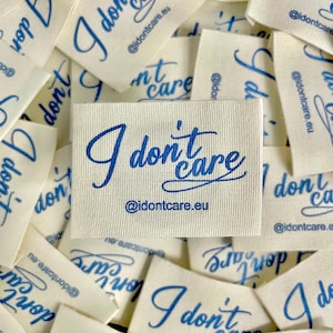 May include: Off-white fabric labels with the phrase "I don't care" in blue script. The labels also include the website address "@idontcare.eu". The labels are scattered, with some overlapping.