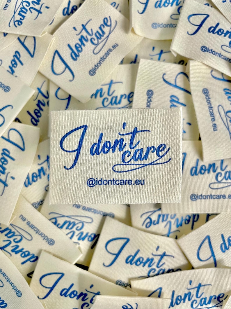 May include: Off-white fabric labels with the phrase "I don't care" in blue script. The labels also include the website address "@idontcare.eu". The labels are scattered, with some overlapping.