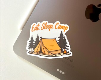 Könnte beinhalten: Ein Aufkleber mit den Worten "Eat. Sleep. Camp" in orangefarbener Schrift. Der Aufkleber zeigt ein orangefarbenes Zelt, zwei dunkelgrüne Kiefern und ein kleines Lagerfeuer. Der Aufkleber befindet sich auf einem grauen Laptop.