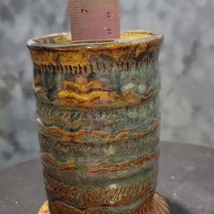 Könnte beinhalten: Handgefertigte Keramikvase mit einem strukturierten, geschichteten Design in Blau-, Braun- und Goldtönen. Die Vase ist etwa 11,4 cm hoch, mit einem dekorativen Sockel und einer zylindrischen Form.