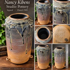 May include: A cylindrical Nancy Kibens Studio Pottery vessel with a blue and yellow drip glaze over a brown base. It features four small side handles and a signed base dated 8/85. A metal ruler shows the height is approximately 9 inches tall.