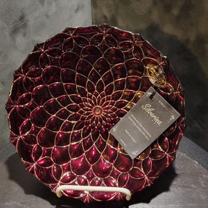以下が含まれることがあります： 金色の花柄が施された、丸いブルゴーニュ色のガラスの装飾皿。 皿には「Silverina」と「Handmade Glass Decorated by Genuine 99% Silver」と書かれたタグが付いています。