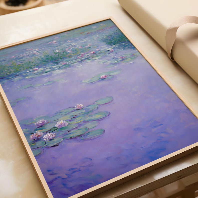 Op de afbeelding: Een ingelijste kunstdruk met een serene waterlelievijver. Het kunstwerk toont een zachte, impressionistische stijl met tinten paars, groen en roze. De waterlelies drijven op het wateroppervlak en het kunstwerk is gevat in een licht houten frame.