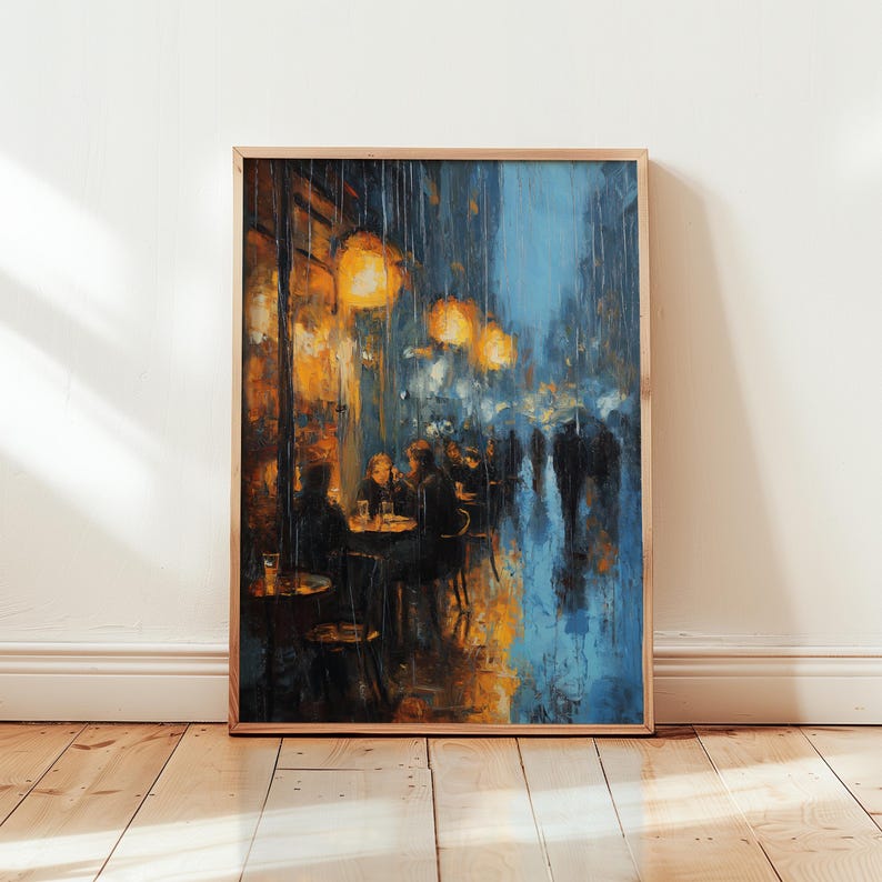 Monet-inspired art poster leaning against a white wall on a wooden floor, sunlight falling across the boards. The painting depicts a rainy café terrace at night, with glowing amber lamps illuminating figures seated at tables. The wet street reflects shades of deep blue and golden orange, painted in textured impressionist strokes that evoke atmosphere and movement. Framed in light natural wood, the print radiates a moody, cinematic feel.