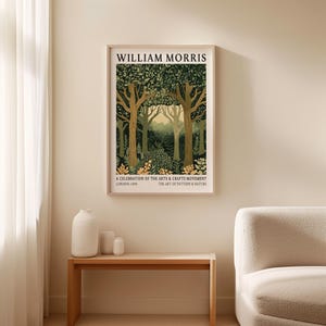 William Morris forest scene art print in a natural wood frame resting on a wooden bench beside minimalist white ceramic vases. The decorative piece shows three tall, graceful trees surrounded by lush foliage and golden flowers, with layers of green forest fading into a hazy yellow horizon. Rendered in the refined Arts & Crafts style, the composition is balanced and richly detailed.