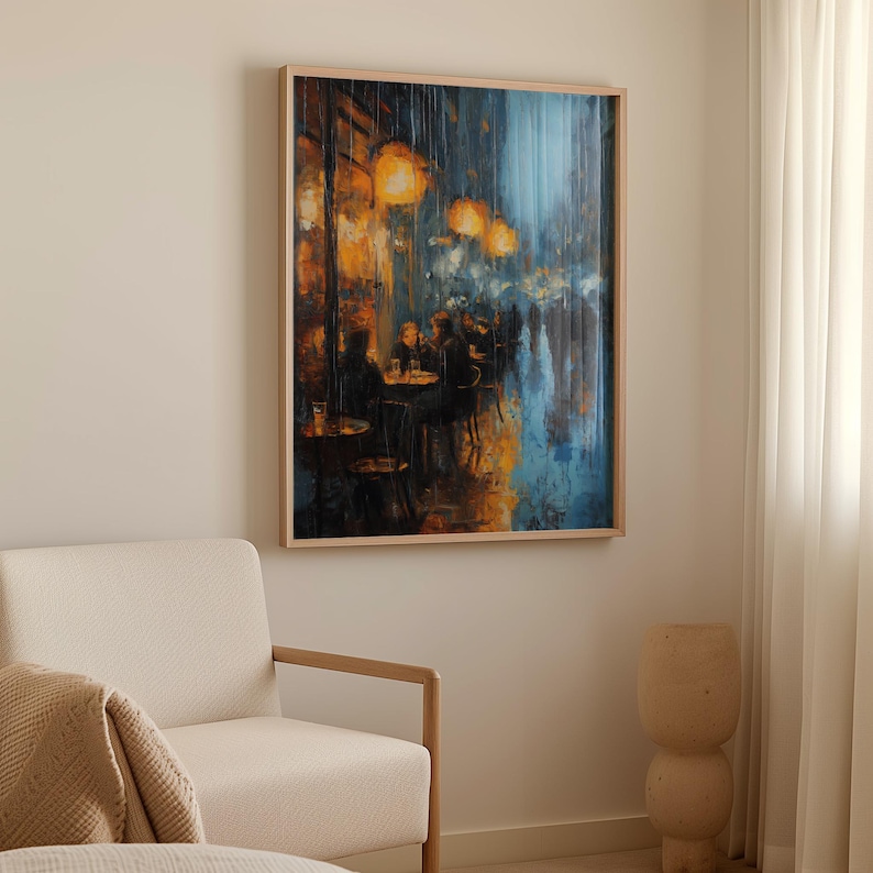 Monet art poster displayed on a pale wall beside a cream armchair and light curtains. The artwork captures a night café scene in the rain, with warm golden lights glowing against a backdrop of deep blues and shadowy silhouettes. The impressionist brushstrokes highlight the rain streaks and glistening reflections, creating an atmospheric urban mood. The natural wood frame enhances the warm contrast within the neutral room.