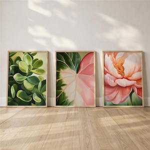 May include: Three framed botanical art prints. The prints feature close-up images of plants and flowers in shades of green, pink, and peach. The frames are a light wood color, and the artwork is displayed on a light wood floor.