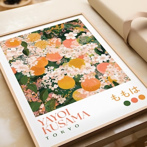 Framed Yayoi Kusama-inspired floral print laid flat on a neutral surface, surrounded by wrapping paper. The detailed design features peach blossoms and fruit with intricate dot patterns and rich greens, pinks, and oranges.