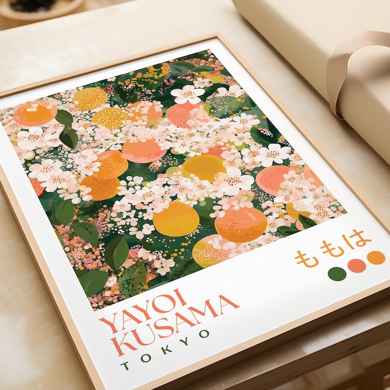 Framed Yayoi Kusama-inspired floral print laid flat on a neutral surface, surrounded by wrapping paper. The detailed design features peach blossoms and fruit with intricate dot patterns and rich greens, pinks, and oranges.