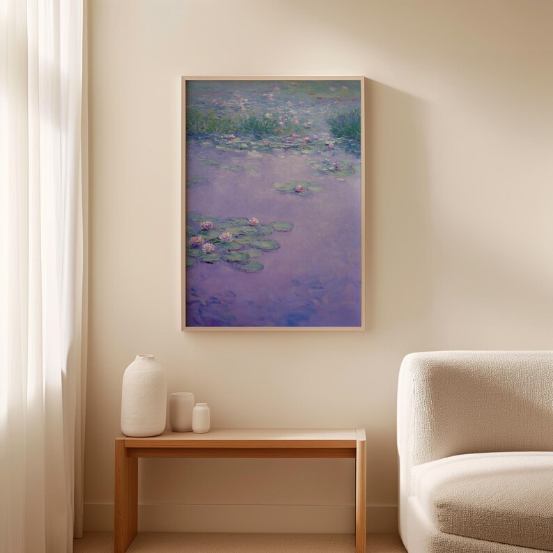 Op de afbeelding: Een ingelijste print van een waterlelievijver, met roze bloemen en groene waterleliebladeren op een paars wateroppervlak. Het kunstwerk zit in een houten lijst en hangt aan een beige muur. Een houten bank en witte vazen staan op de voorgrond.