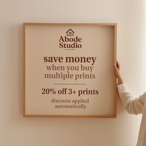 Abode Studio promotional sign offering 20% off when you buy 3 or more prints, with text reading ‘save money when you buy multiple prints’ and ‘discount applied automatically,’ held by a person in a minimalist setting